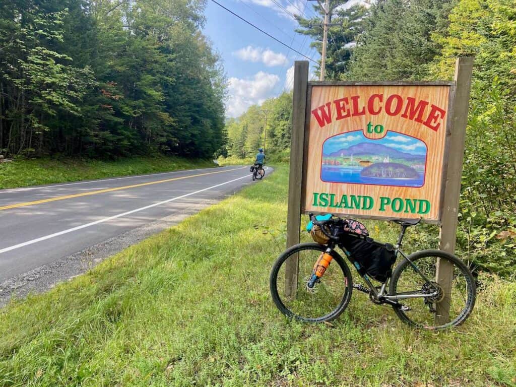 Loaded bikepacking bike leaning against Island Pond welcome sign in Vermont