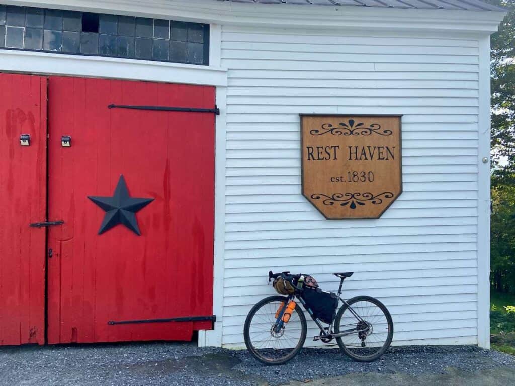 Bike loaded with bikepacking bags leaning against barn wall with sign that says "Rest Haven est. 1830"