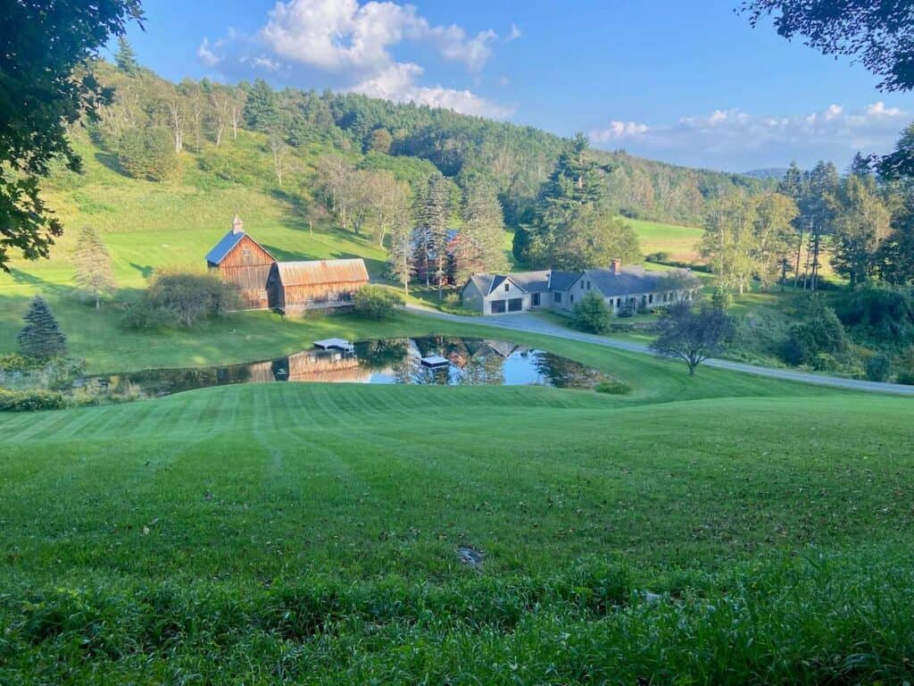 Pastoral Vermont scene of rolling green hills and idyllic farmhouse set behind a pond