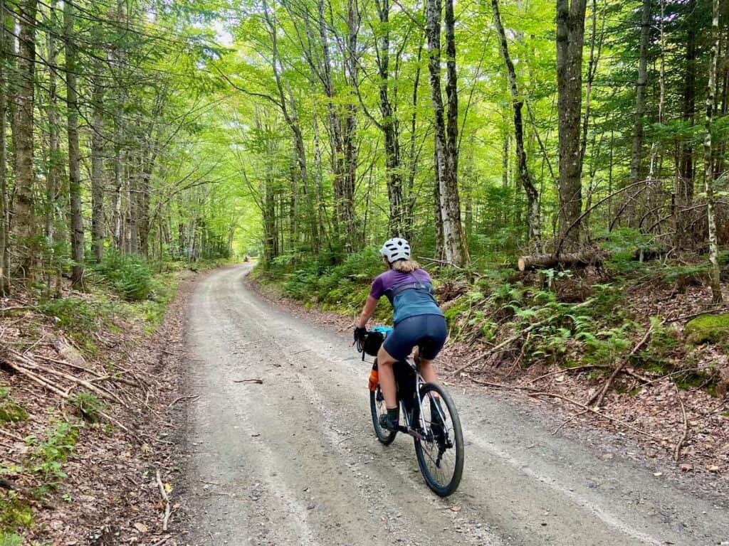 Cyclist riding bike on gravel road on the VTXL route in Vermont with forest on either side