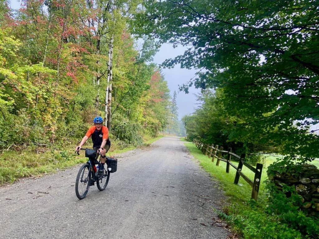 Man riding bike on scenic gravel road in Vermont lined with early season fall foliage.