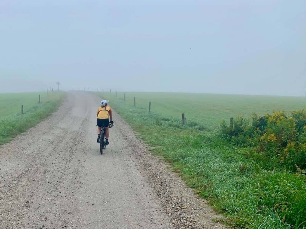 Woman riding gravel bike on dirt road in Vermont in misty morning