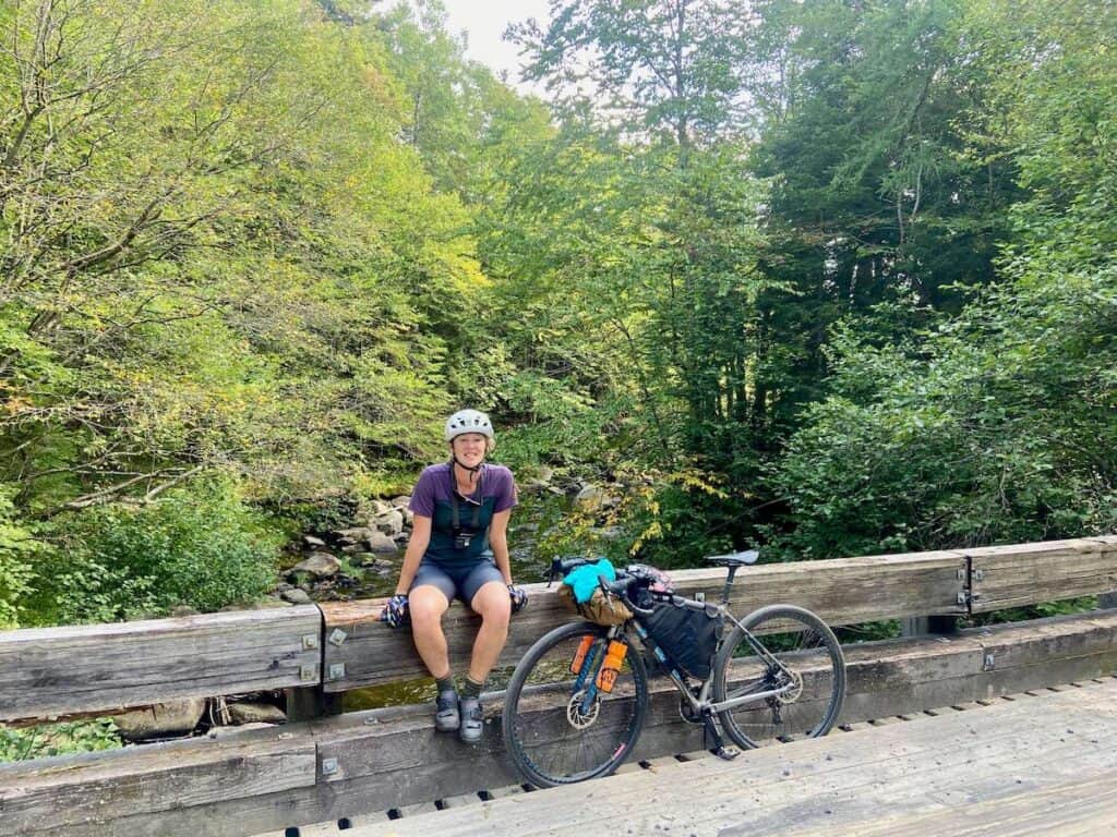 Bikepacker sitting on edge of wooden bridge next to bike on VTXL gravel bikepacking route in Vermont
