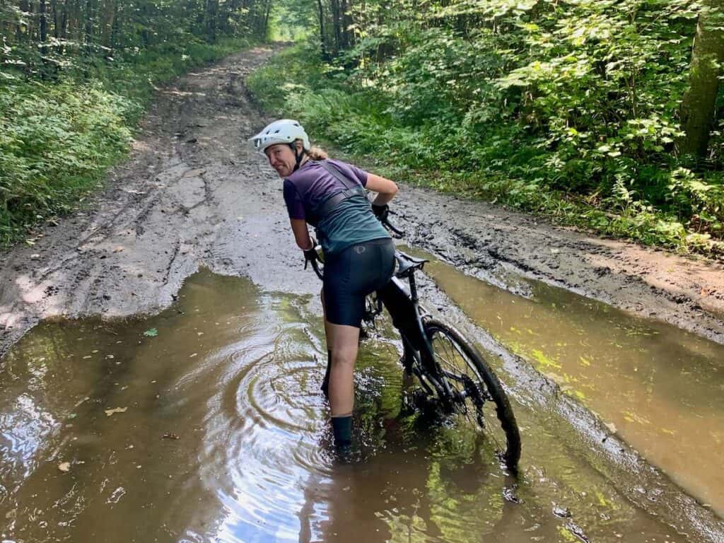 Woman pushing bike through a mud puddle on class 4 road in Vermont