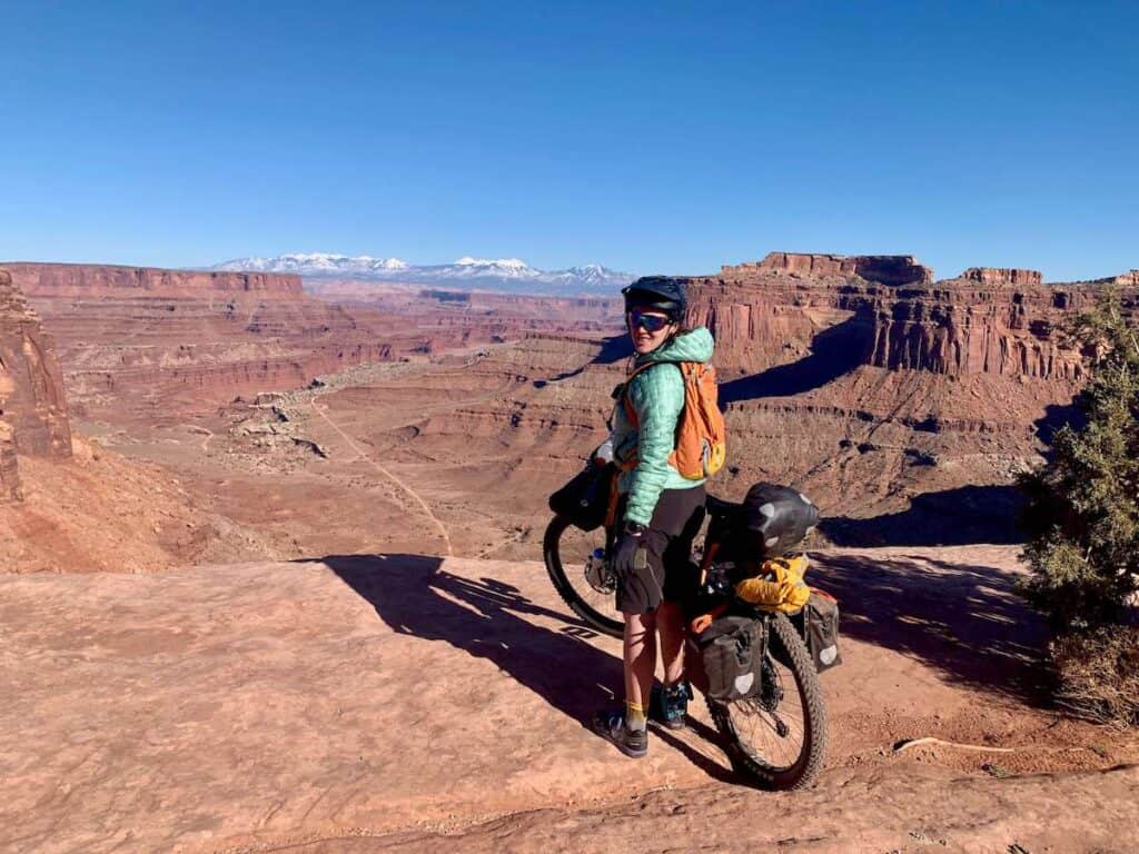 Woman standing next to bikepacking bike at scenic overlook on the White Rim Trail in Moab