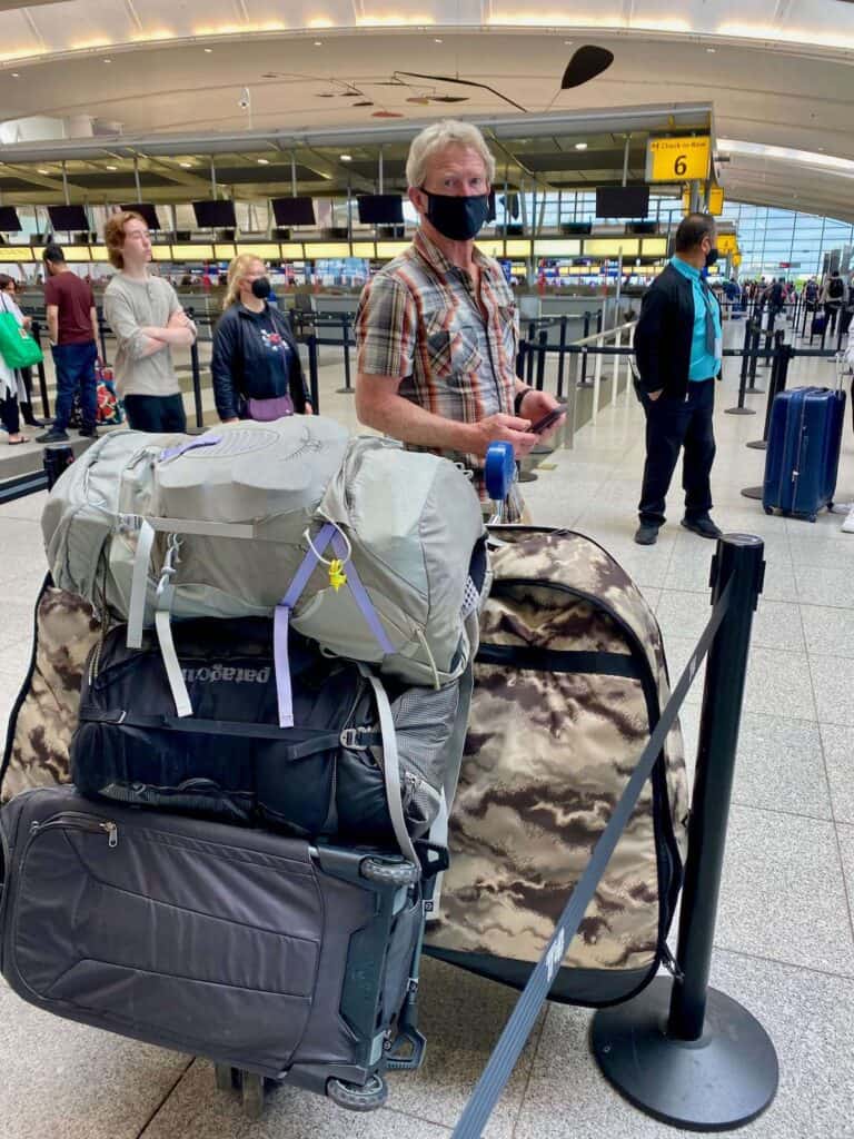 Man standing next to airport cart loaded with bike bags and luggage