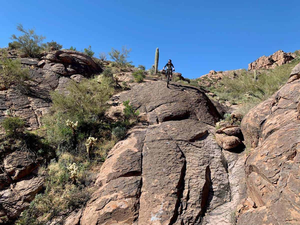 Mountain biker riding bike down steep rock slab at Gold Canyon in Phoenix, Arizona
