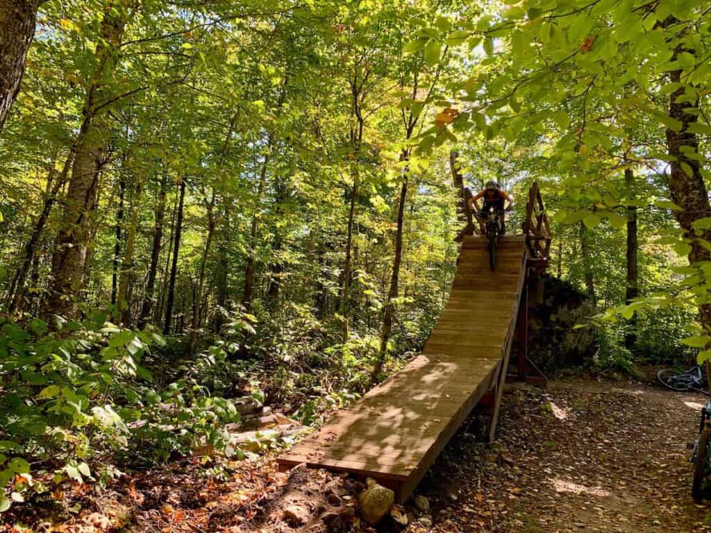 Mountain biker riding down steep wooden ramp on trail network in Quebec