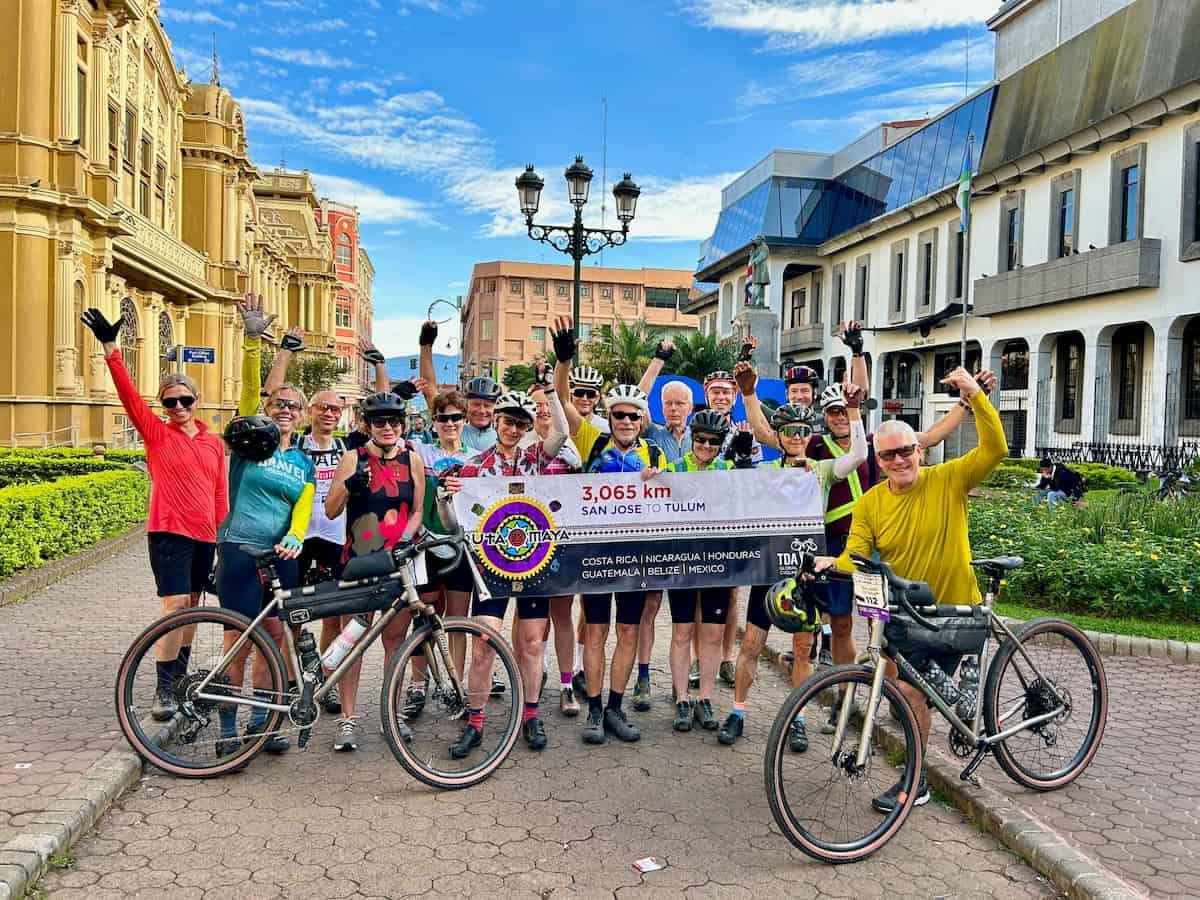 Group of cyclists posing for photo with banner for the Ruta Maya bicycle tour