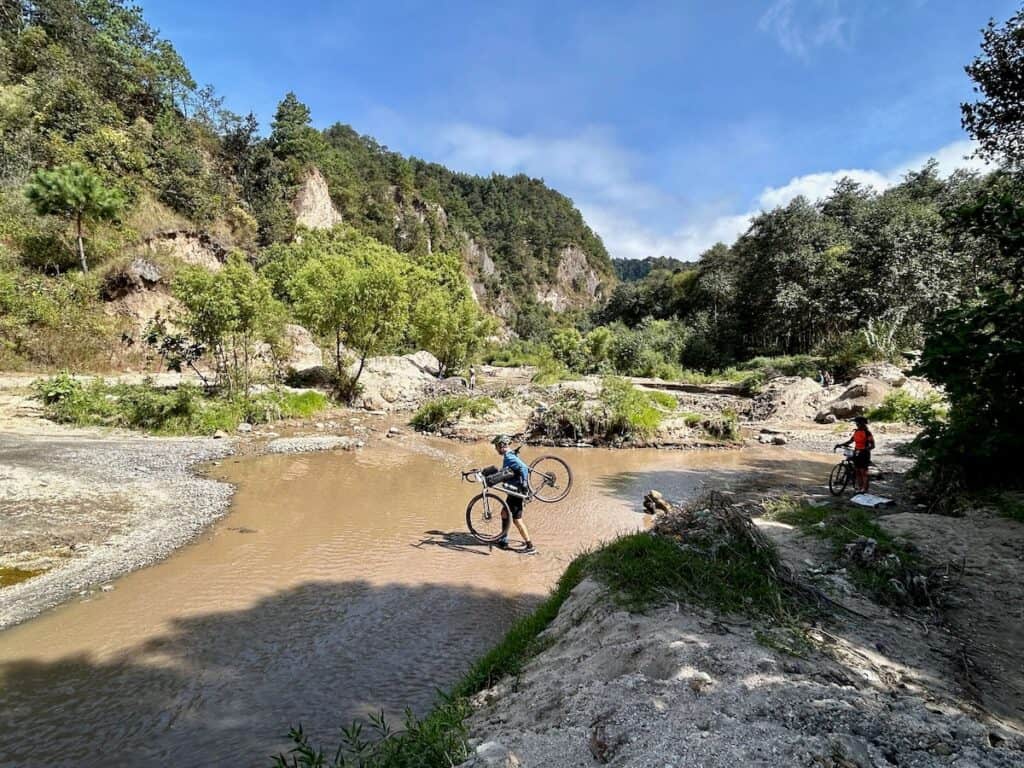 Many carrying bike across shallow river in canyon in Guatemala