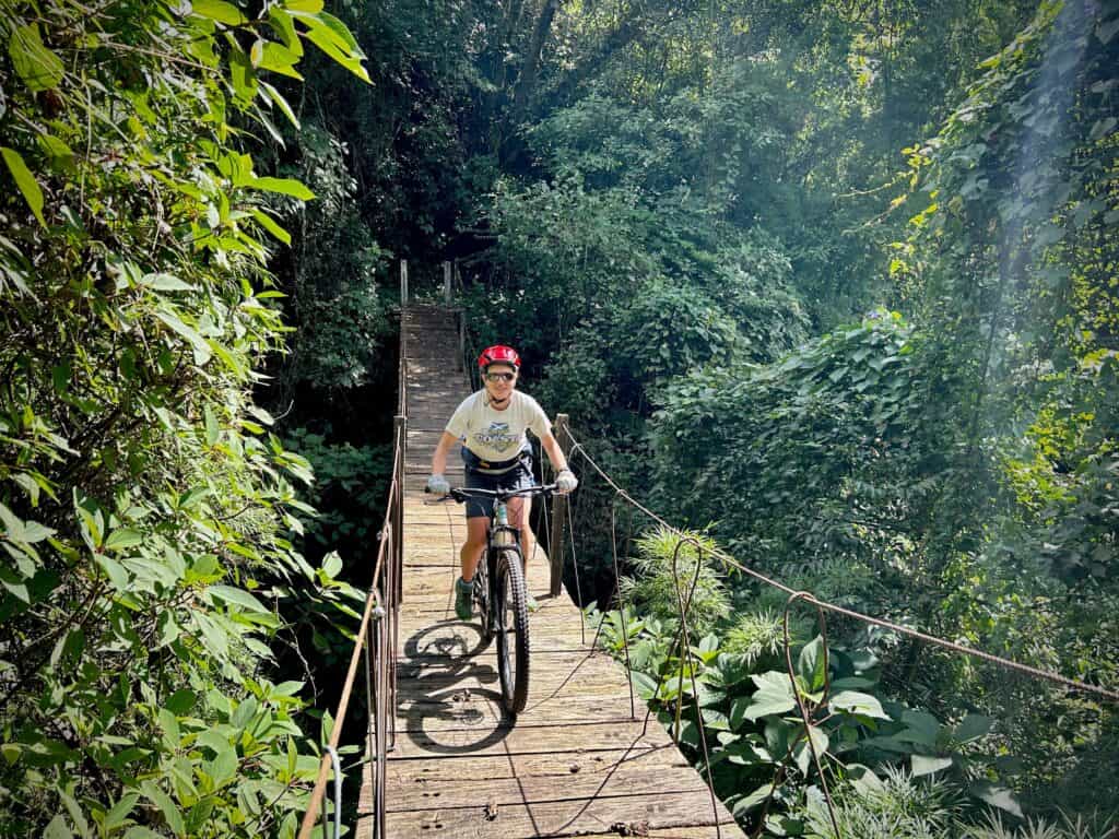 Female mountain bike riding bike over a suspension bridge on a trail down a volcano in Guatemala