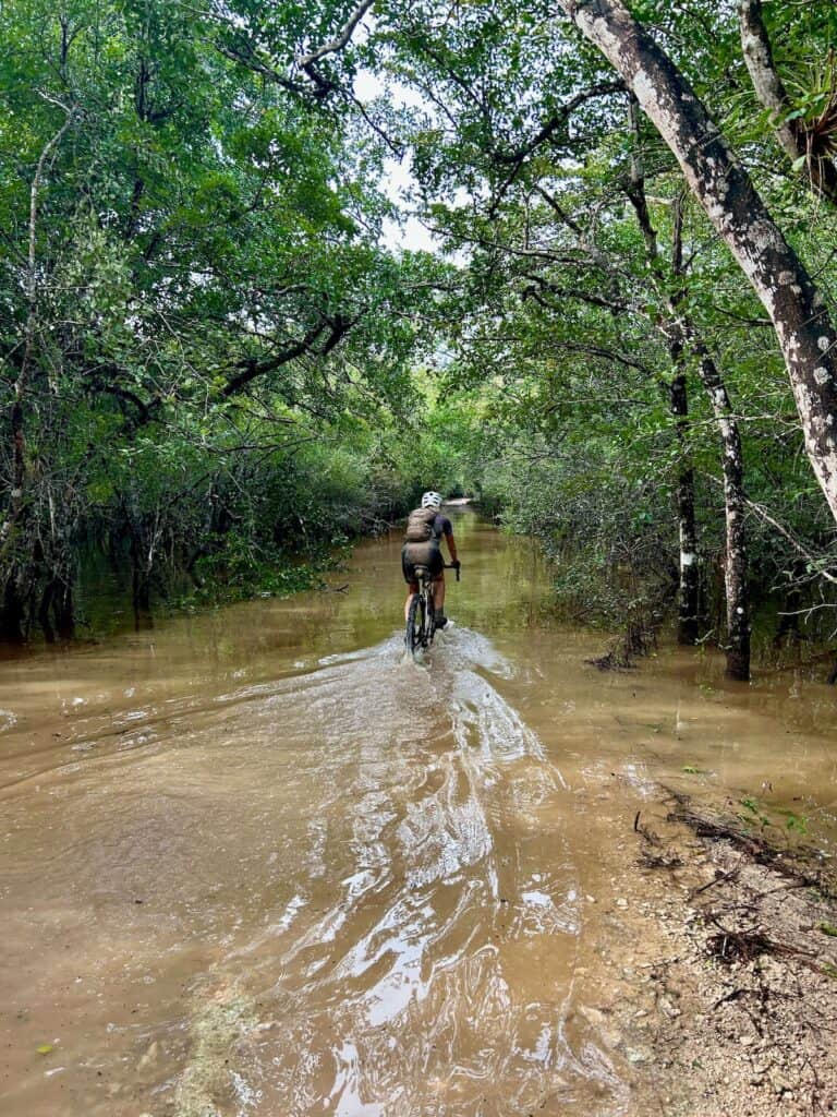Woman riding bike through flooded section of road through the jungle in Mexico