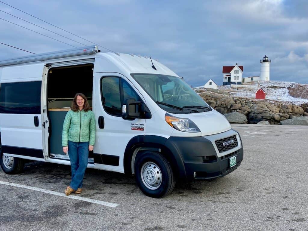 Woman standing in front of converted campervan with lighthouse in the background