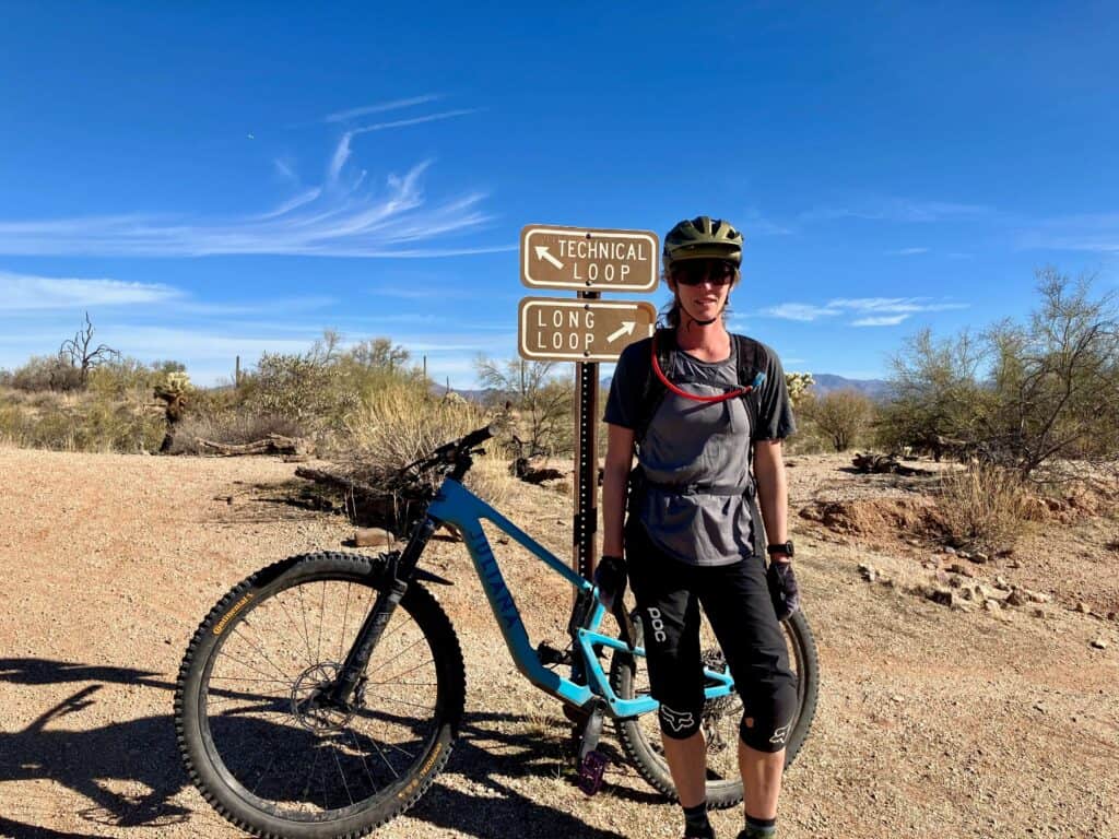 Female mountain biker standing next to bike and trail sign at McDowell Mountain Regional Park in Phoenix