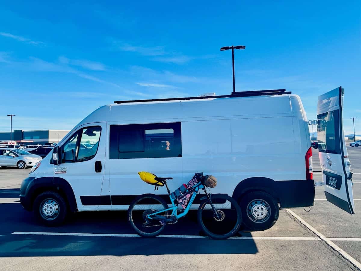 Loaded bikepacking bike leaning against white van in parking lot
