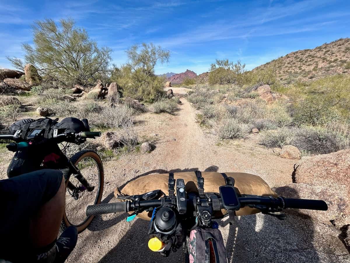 Photo out over front of bike loaded with handlebar bag and bikepacking gear onto desert trail
