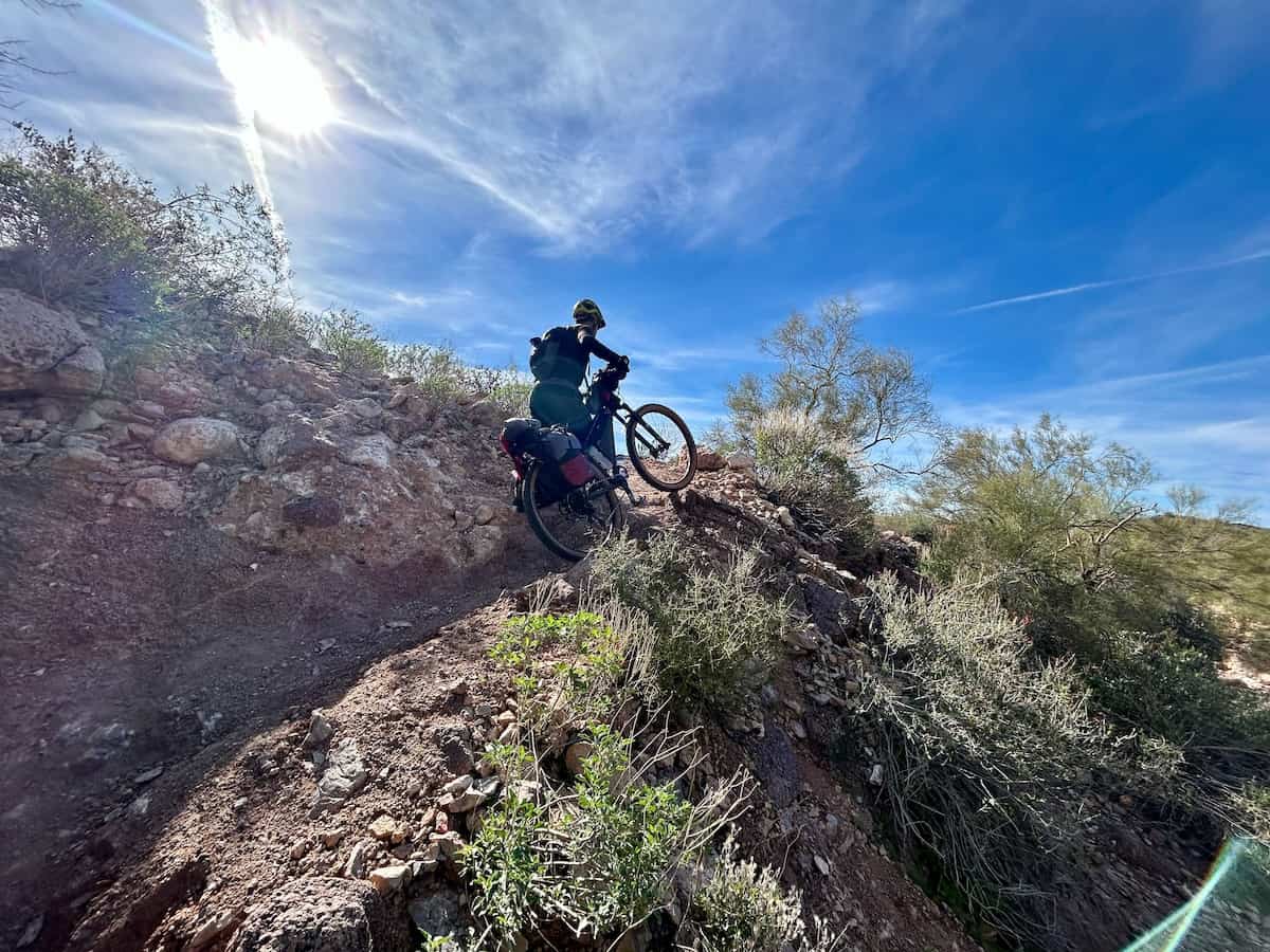 Bikepacker pushing loaded bike up a steep section on trail on the Queen's Ransom bikepacking route in Arizona