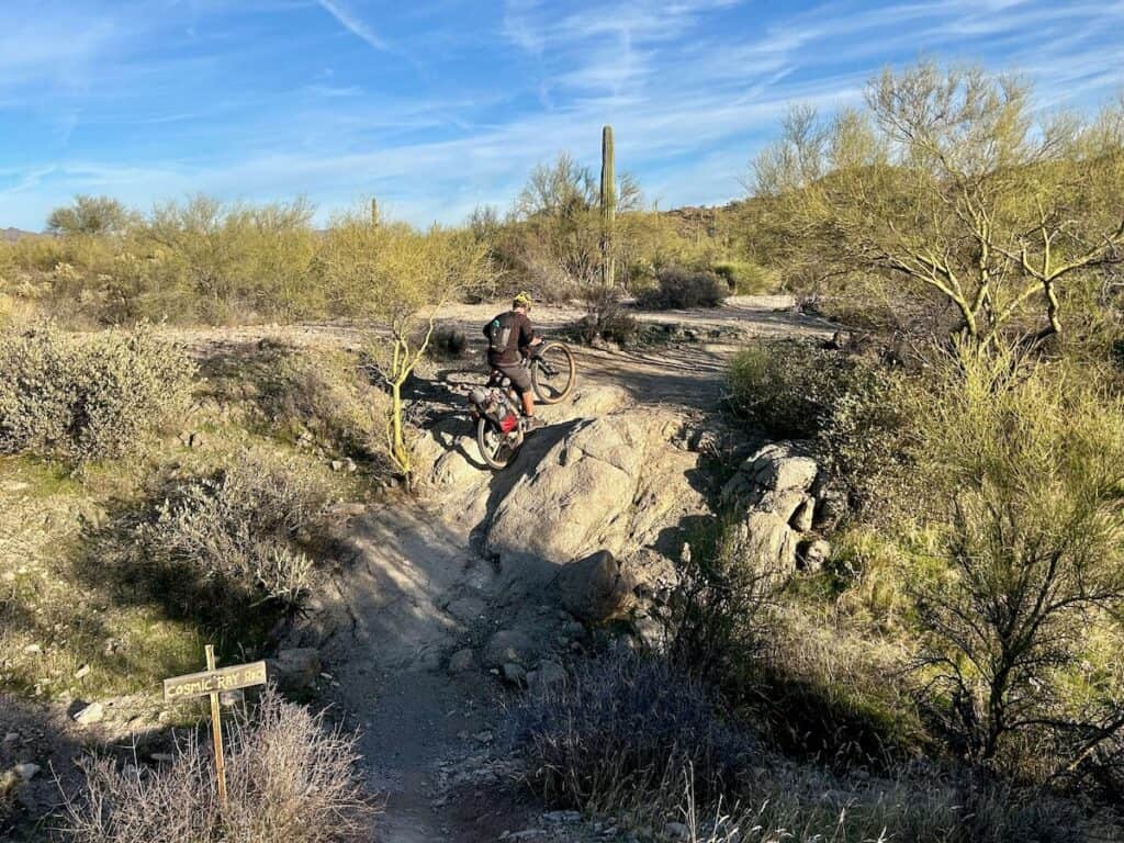 Bikepacker riding bike up steep side of a wash on a trail in Phoenix, Arizona