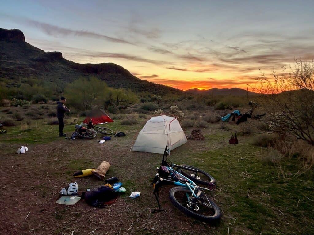 Bikepackers setting up camp at wild dispersed campsite at sunset