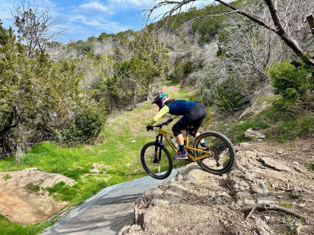 Mountain biker riding bike down rock ledge onto a wooden ramp wearing a Smith Mainline full face helmet