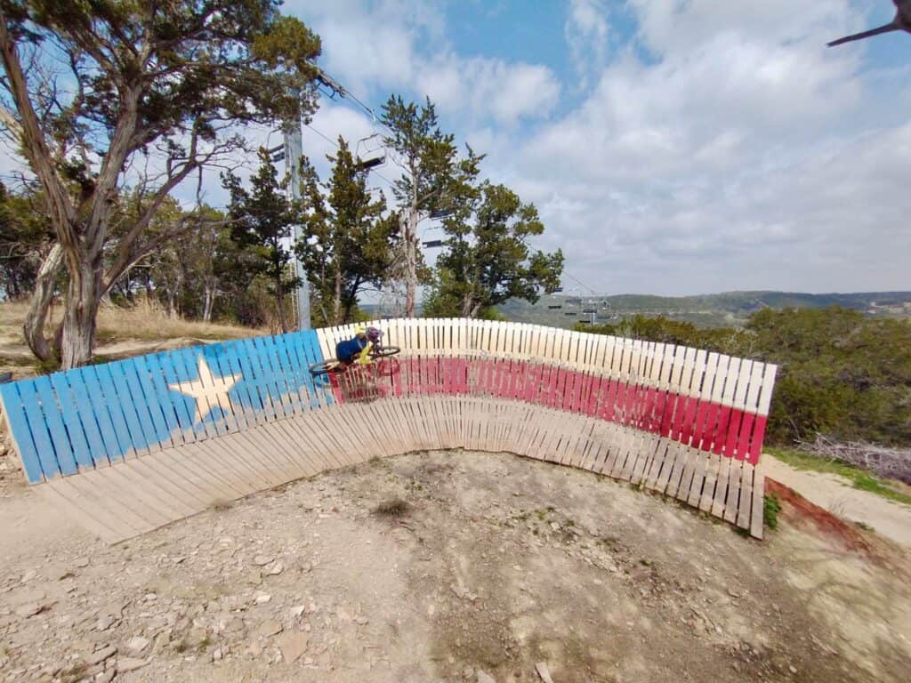 Mountain biker riding wooden wall ride painted like the Texas flag at Spider Mountain Bike Park