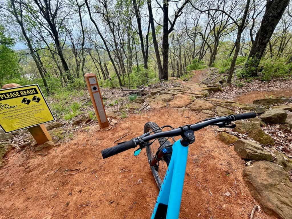 Photo out over front of mountain bike handlebars onto red dirt trail at Centennial Park in Fayetteville, Arkansas