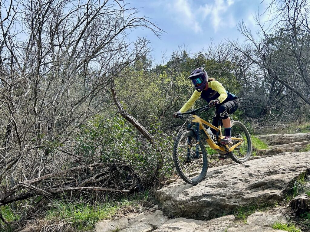 Mountain biker wearing a full face helmet riding bike down a steep rocky section on trail