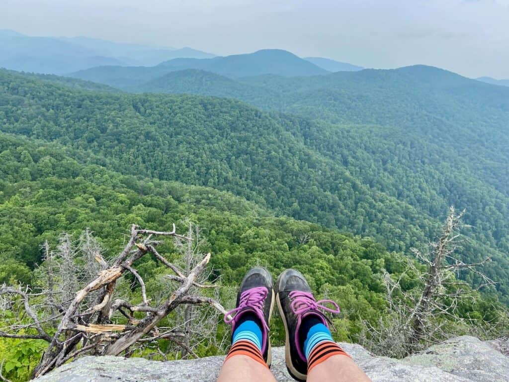 Photo out over persons shoes and colorful socks onto green mountain landscape
