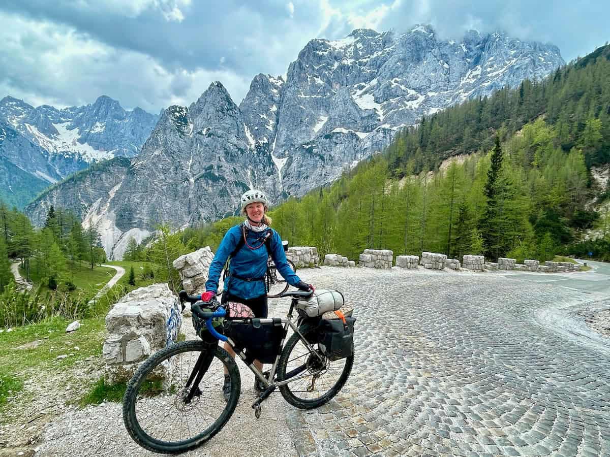 a woman standing on a bicycle in front of a mountain